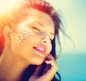 Beautiful happy cute Girl applying Sun Tan Cream on her Face over ocean background