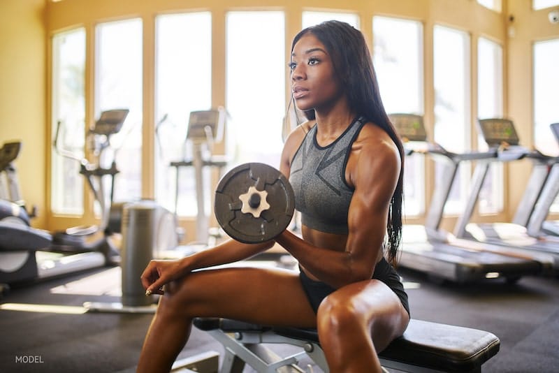 Very fit young woman lifting dumbbell weights in gym.