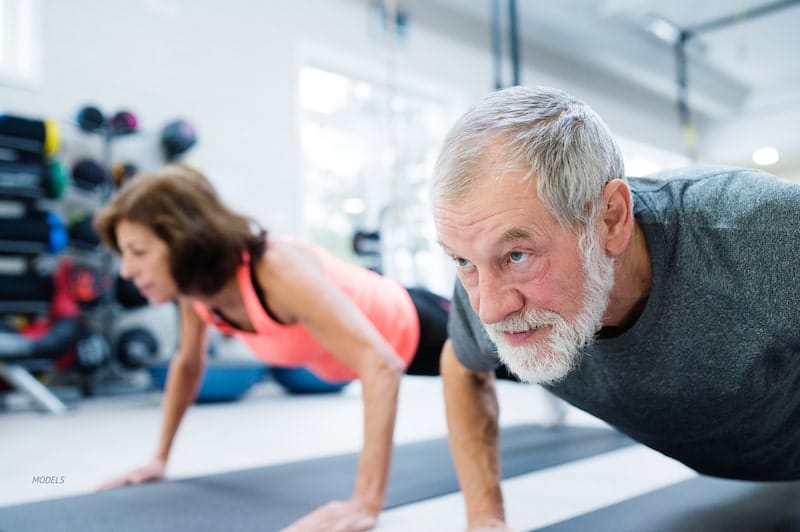 Middle aged man and woman stretching in a gym.