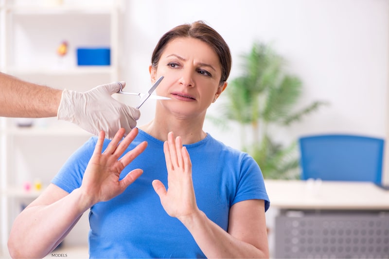 Woman nervously moving away from surgeon's scissors