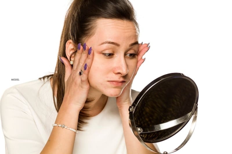 Young woman looking in the mirror as she pulls her facial skin tight.