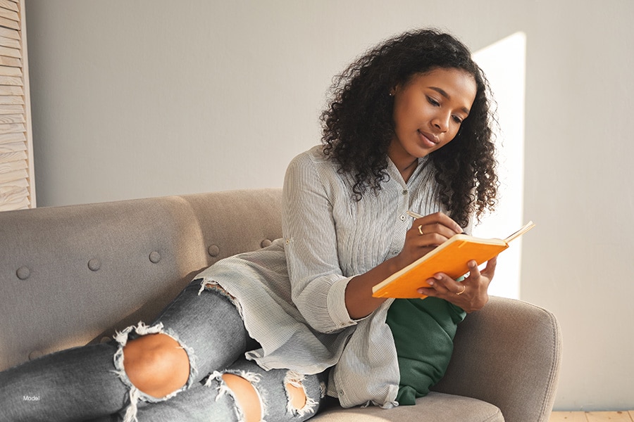 Woman sitting on a couch writing in a journal